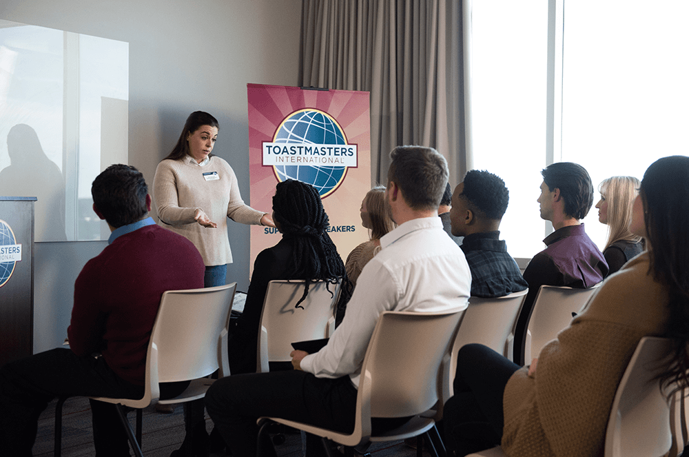 Woman giving speech in front of audience with Toastmasters banner and lectern in background