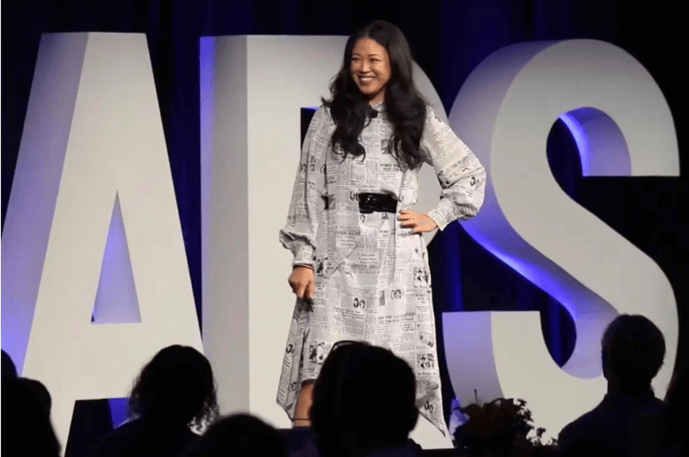 2024 Toastmasters Golden Gavel recipient Lisa Sun speaking onstage in white dress with hand on hip