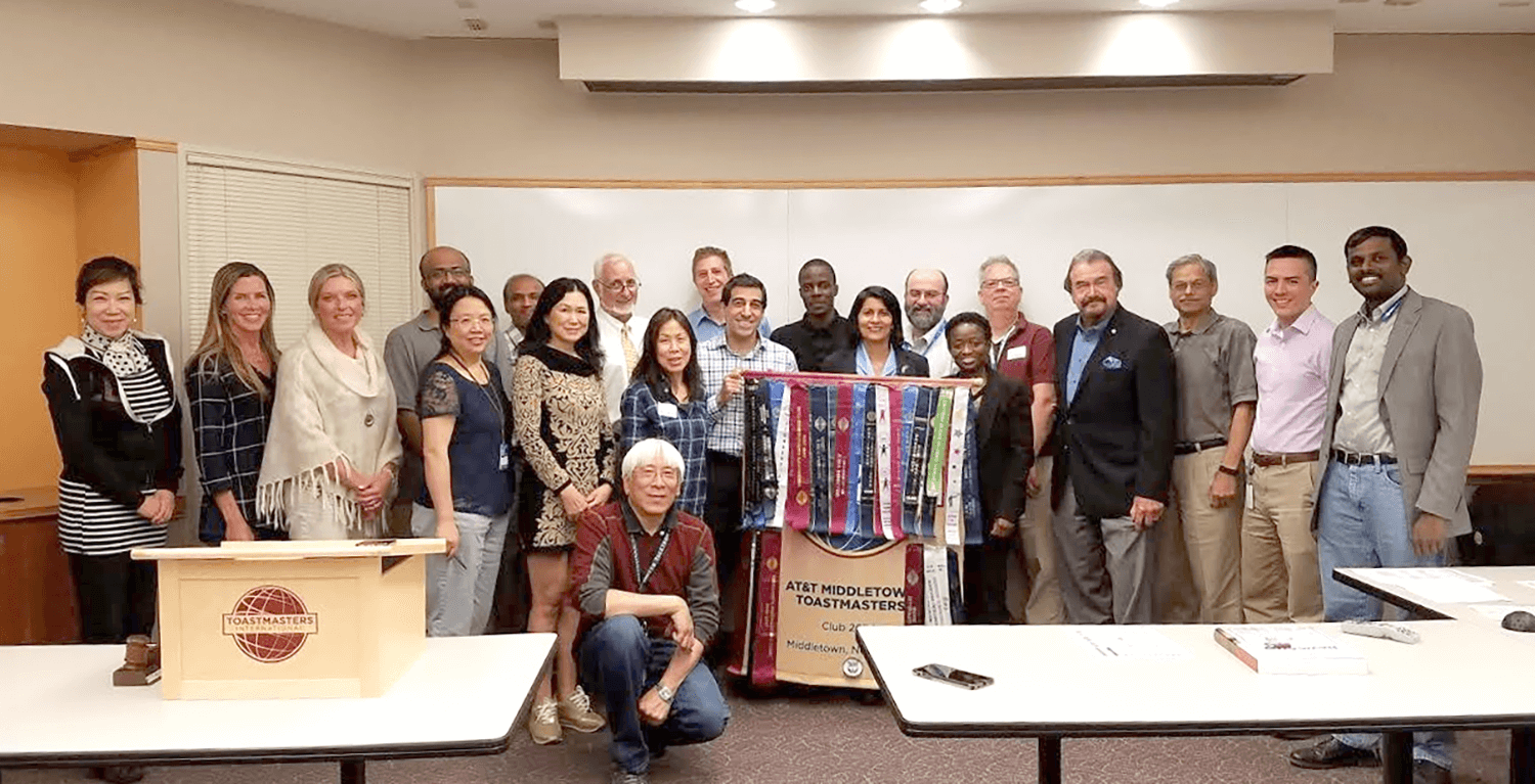 Spear (behind banner) poses with her home club AT&T Middletown Toastmasters of Middletown, New Jersey. The club has been President’s Distinguished for 15 years in a row.