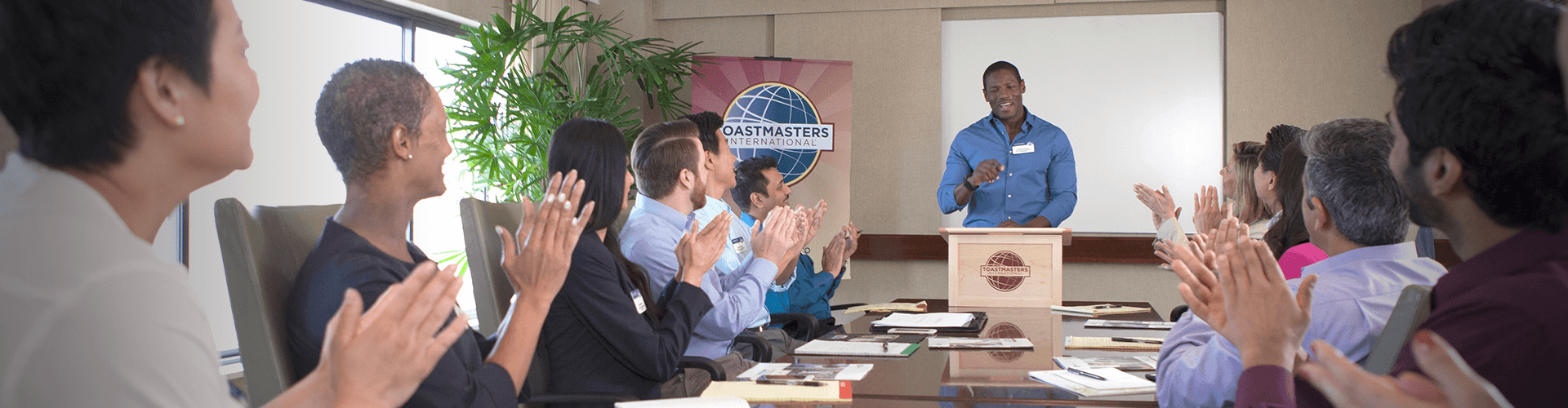 Man standing at lectern speaking while people clap at table