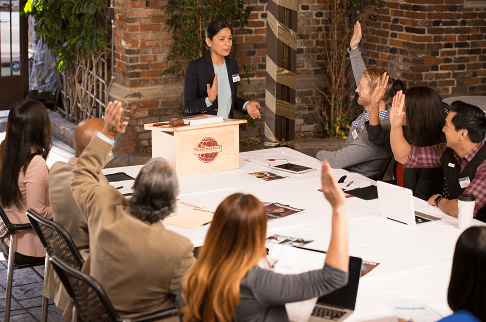 Woman speaking at lectern to people with raised hands