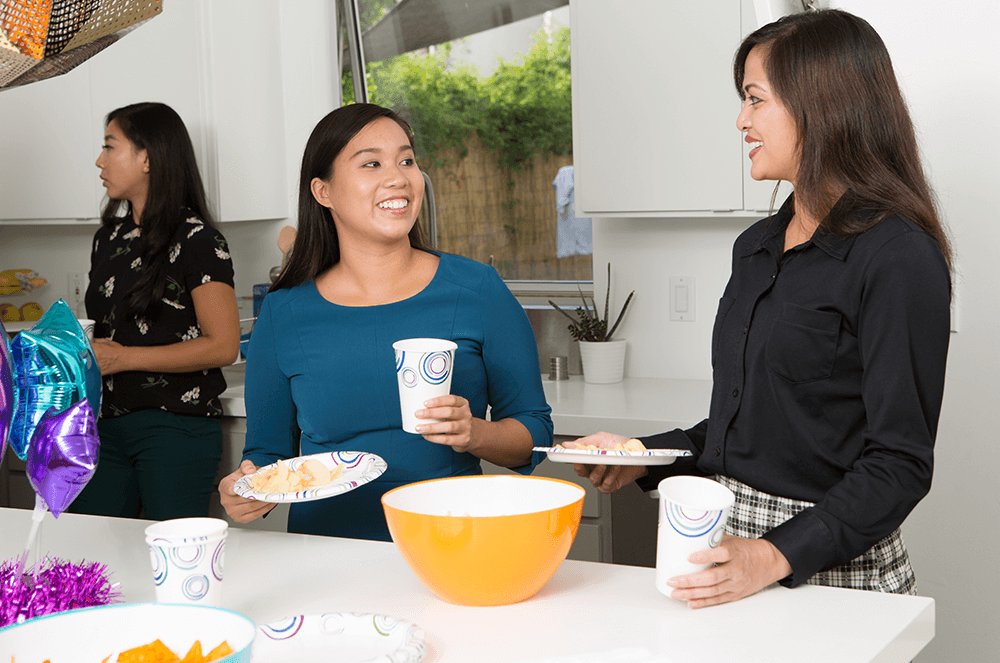 Two women smiling while holding plates of food and cups