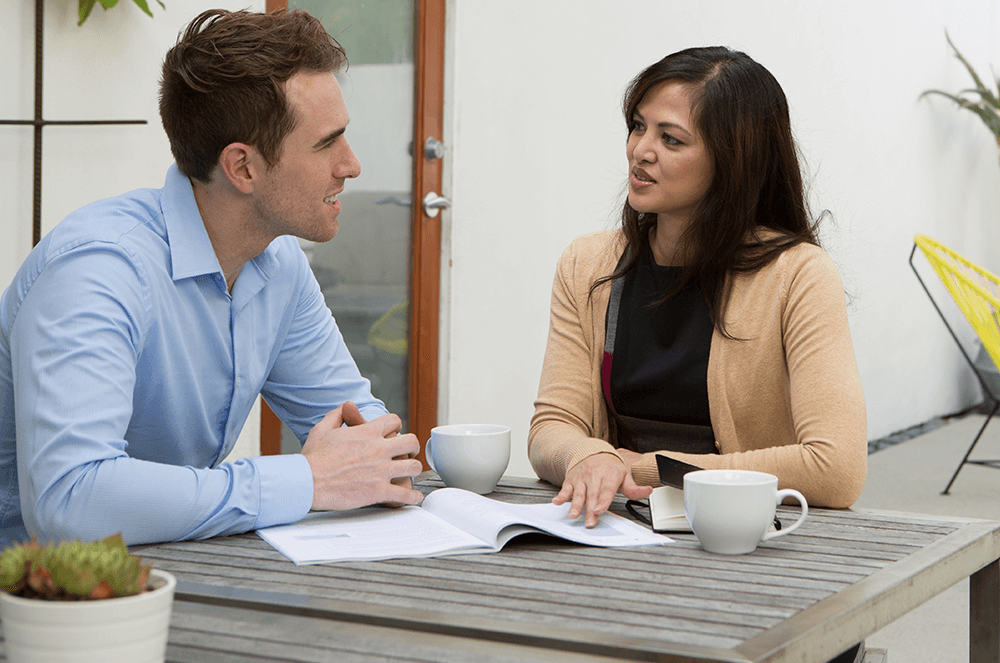 Woman and man speaking at table with coffee mugs