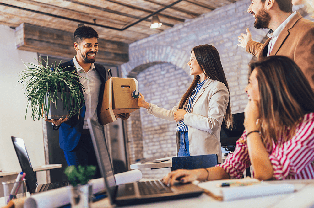 Man starting new job with box and plant while coworkers smile