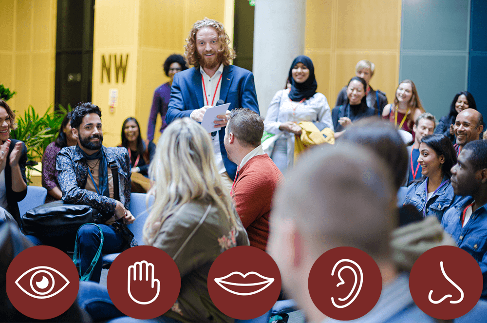 Man in blue jacket speaking to audience with maroon icons showing five senses