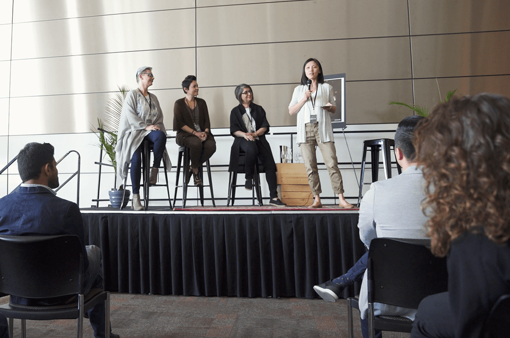 Woman moderating a panel of three people with audience watching 