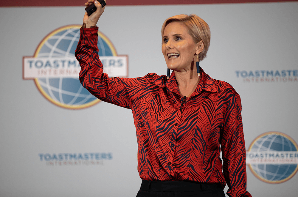 Woman in red shirt with arm up speaking onstage