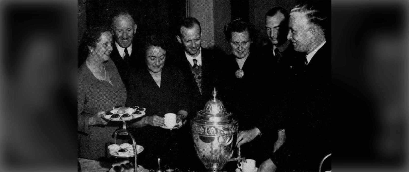 Black and white image of men and women enjoying tea and pastries