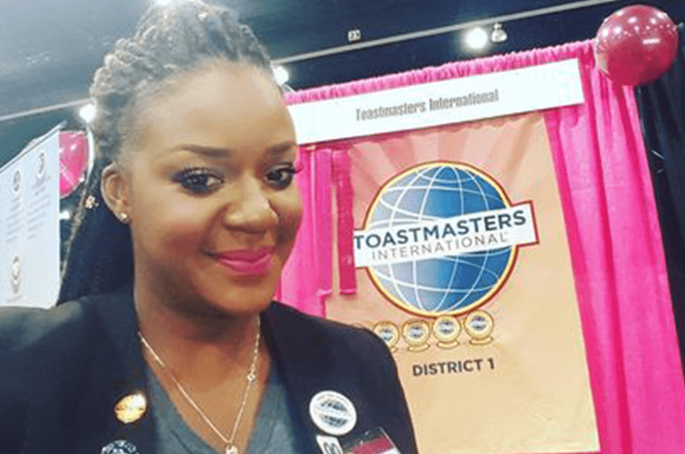 Woman in black jacket with Toastmasters t-shirt and pins and badges