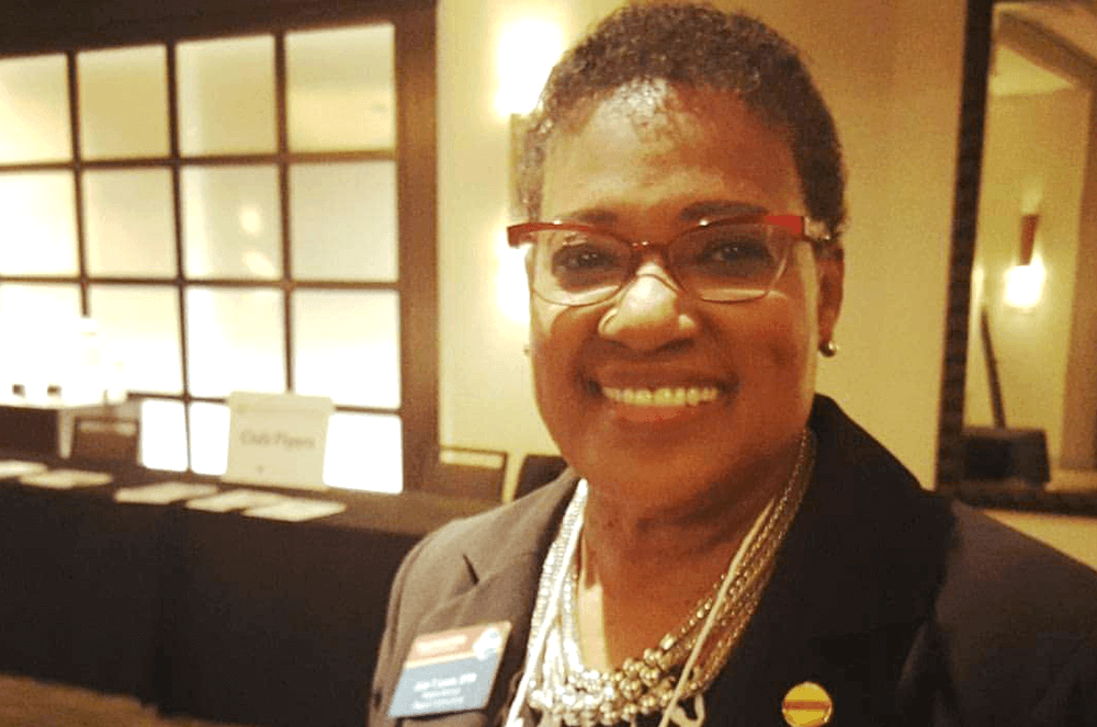 Woman smiling in black jacket with Toastmasters pin and badge