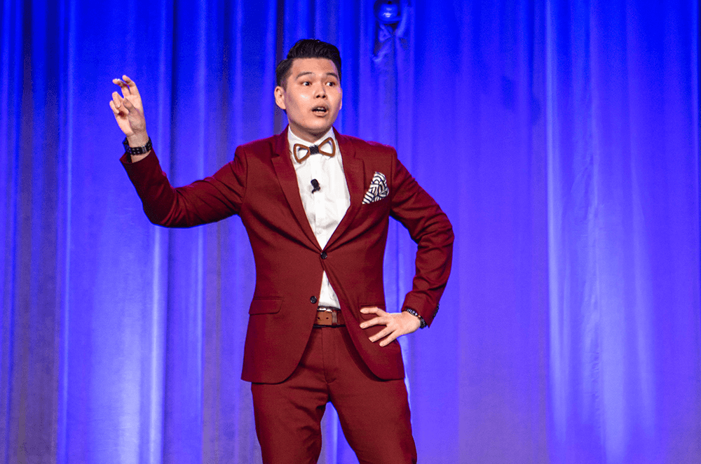 Man in red suit jacket speaking onstage with hand in air