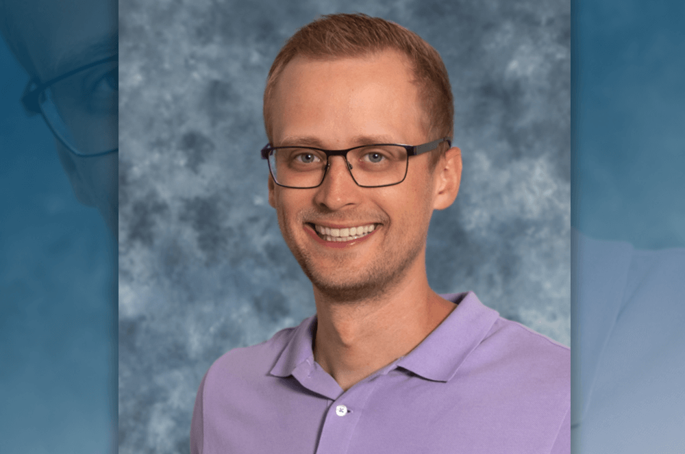 Man in purple shirt and glasses posing with blue background