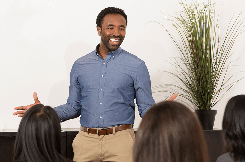 Man in blue button-down shirt speaking with gestures as audience watches