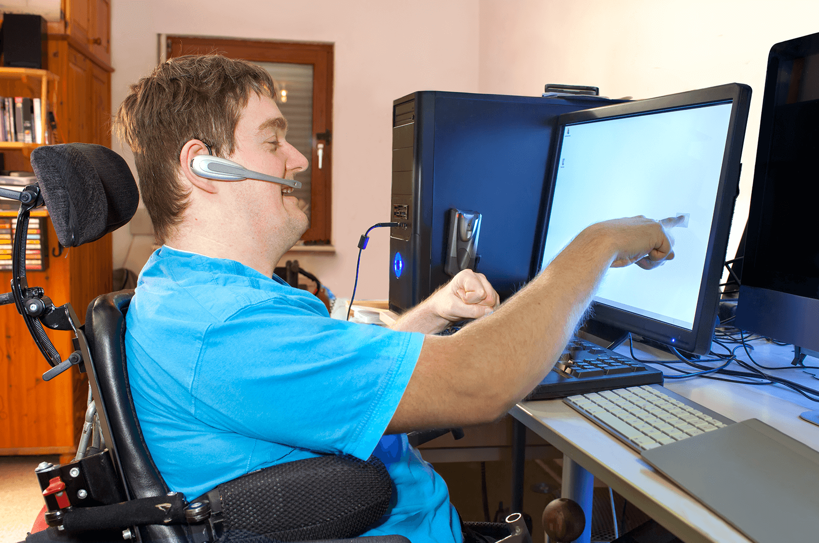 Man wearing blue shirt sitting in wheelchair pointing at computer screen