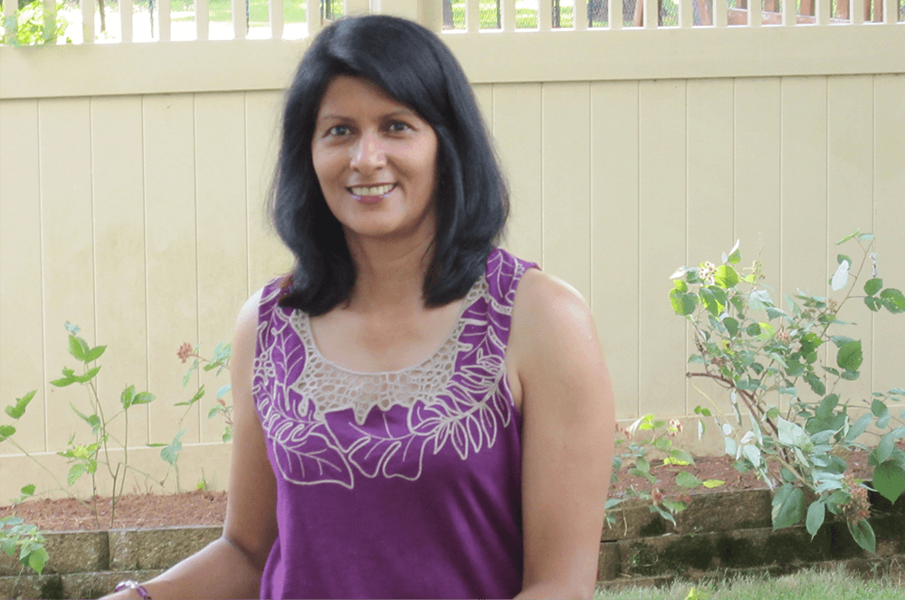 Woman in purple shirt posing in garden with white fence and plants