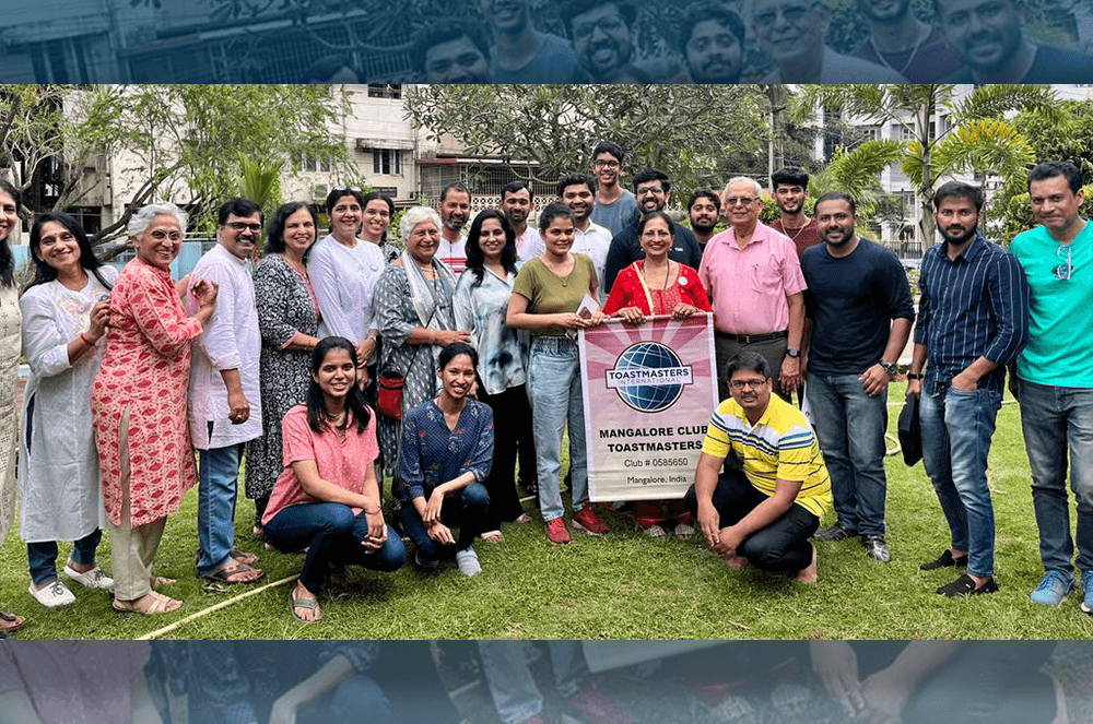 Group of people posing outdoors with Toastmasters banner