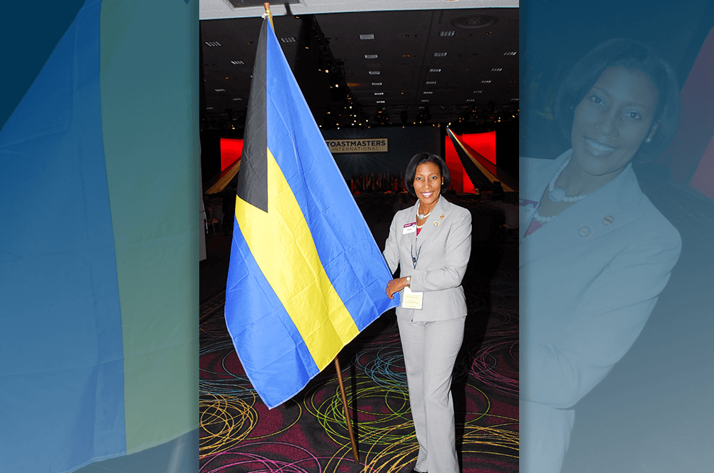 Rolle, who currently lives and works in The Bahamas, poses next to the flag of The Bahamas at a past Toastmasters convention.