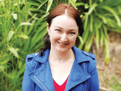 Jolene Stockman smiles in red shirt and blue jacket outside