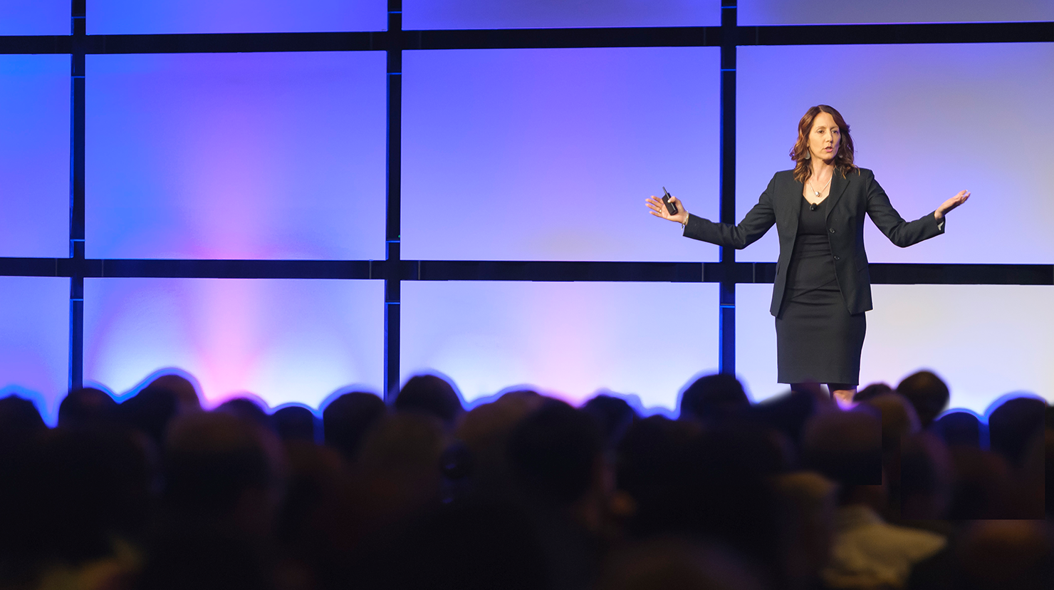 Woman speaking onstage with hands up