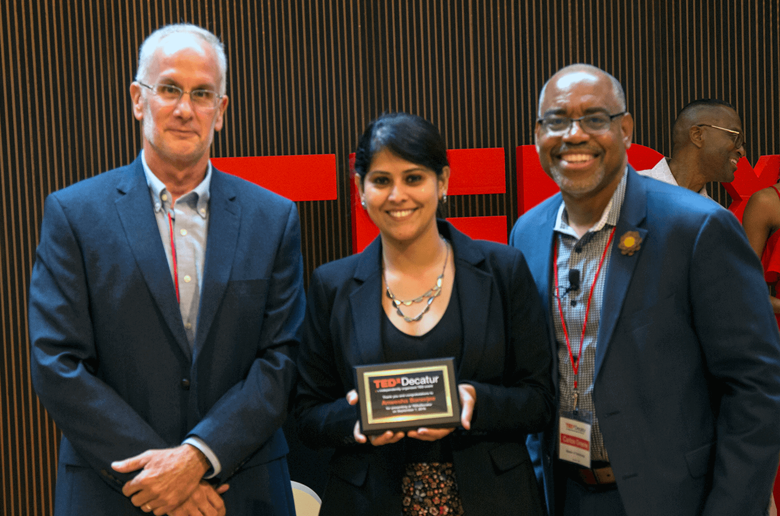 Anwesha Banerjee stands in between Toastmasters Carlos Greene and Daniel Enger while holding a plaque