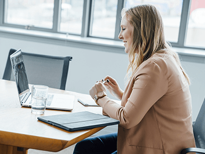 Woman in tan sweater sitting at a desk smiling at someone on her laptop