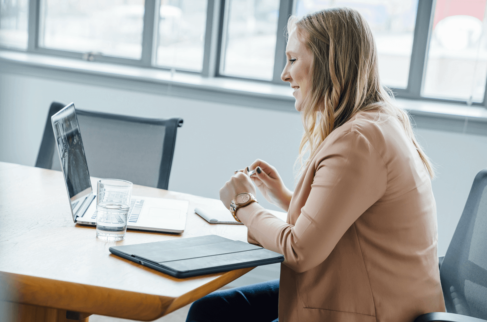 Woman in tan sweater sitting at a desk smiling at someone on her laptop