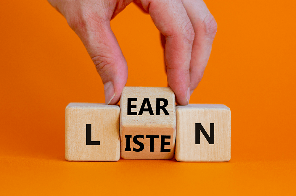 Hand holding block with letters that spell out learn and listen with orange background